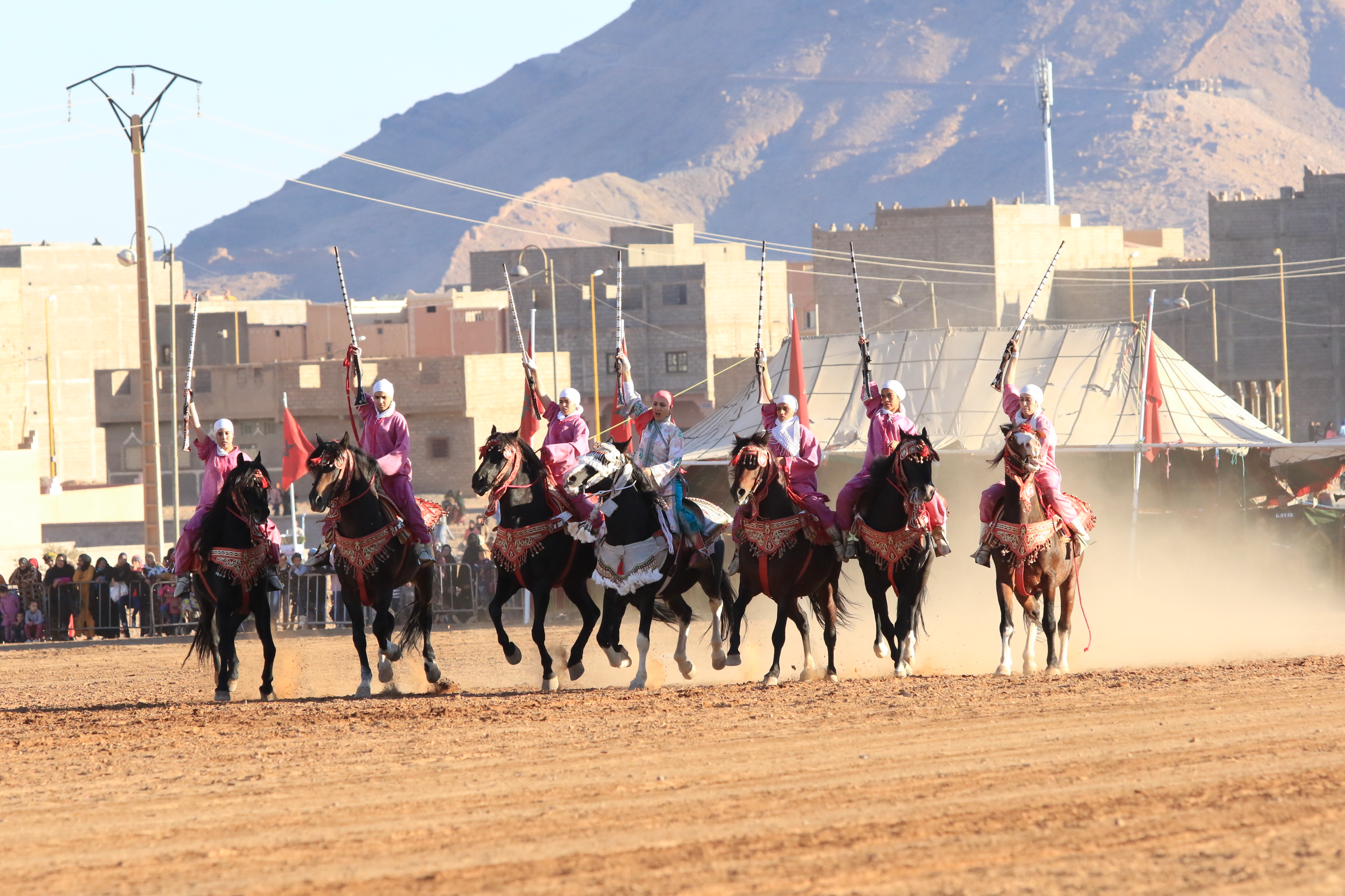 Group of women on horses gallop together. Dust is being kicked up behind them.