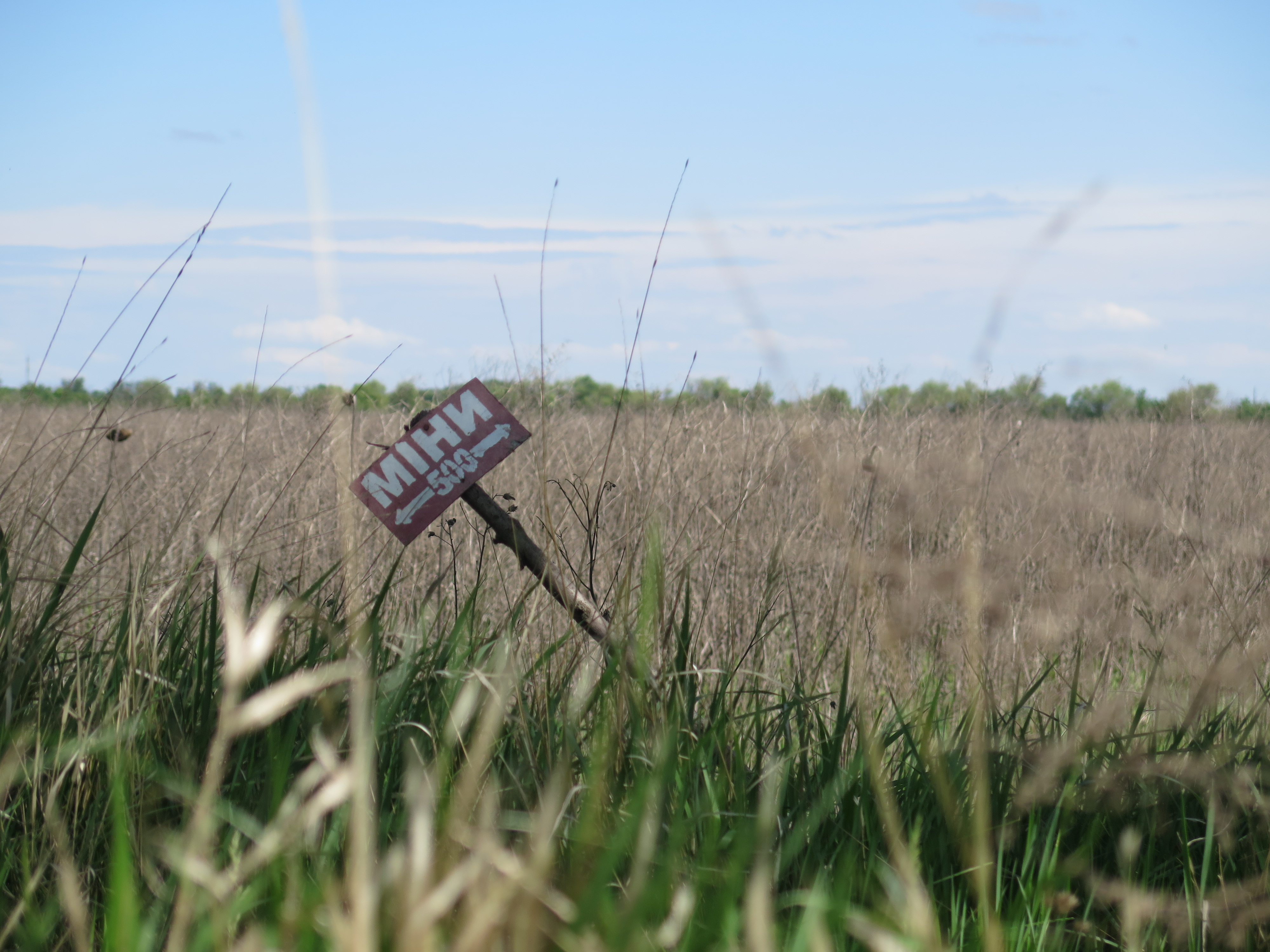 A photograph of a vast field and blue sky. A sign in the field reads "MIHИ 500."" 