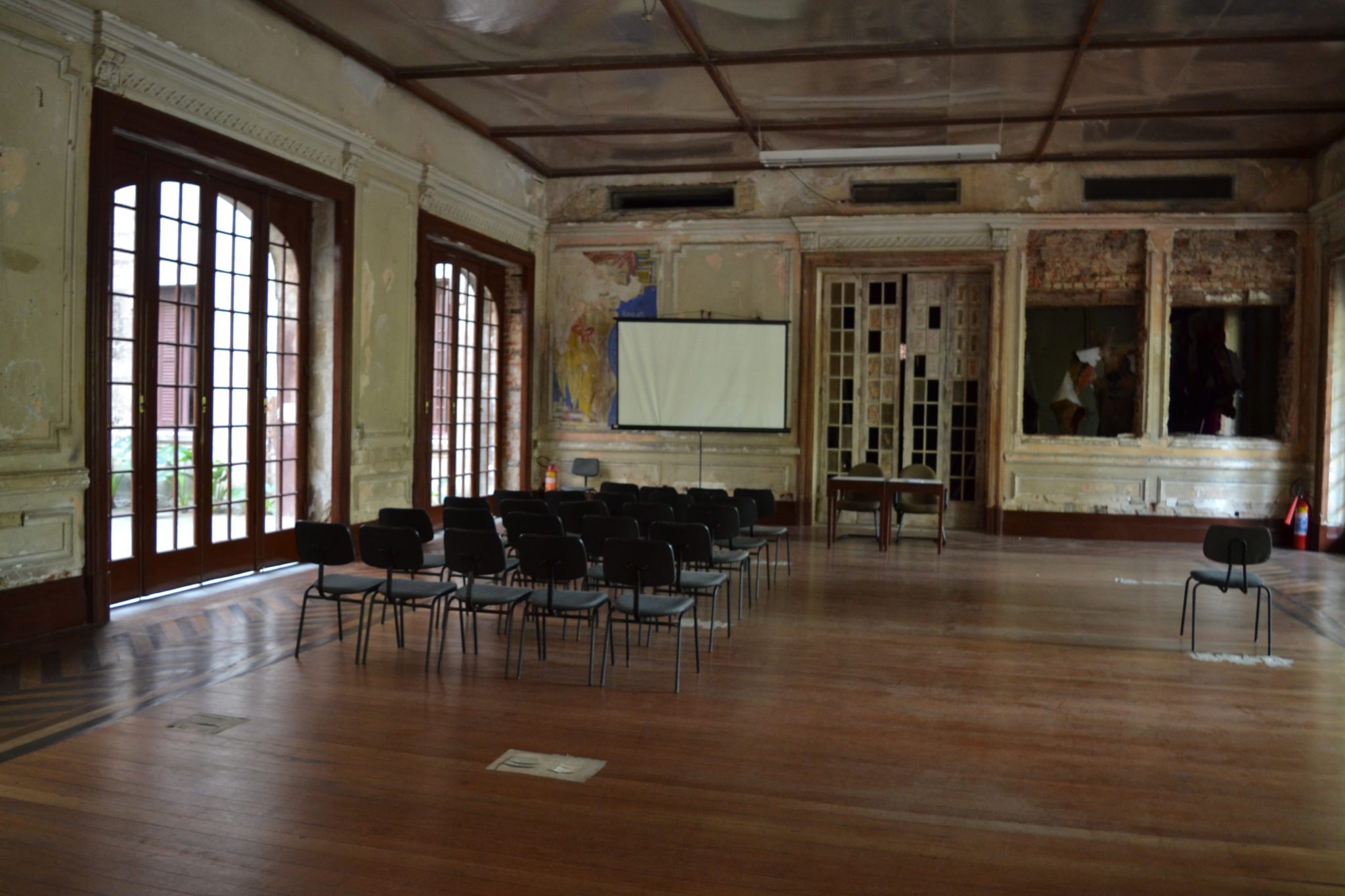 An old, empty meeting room with black chairs and a projector screen.