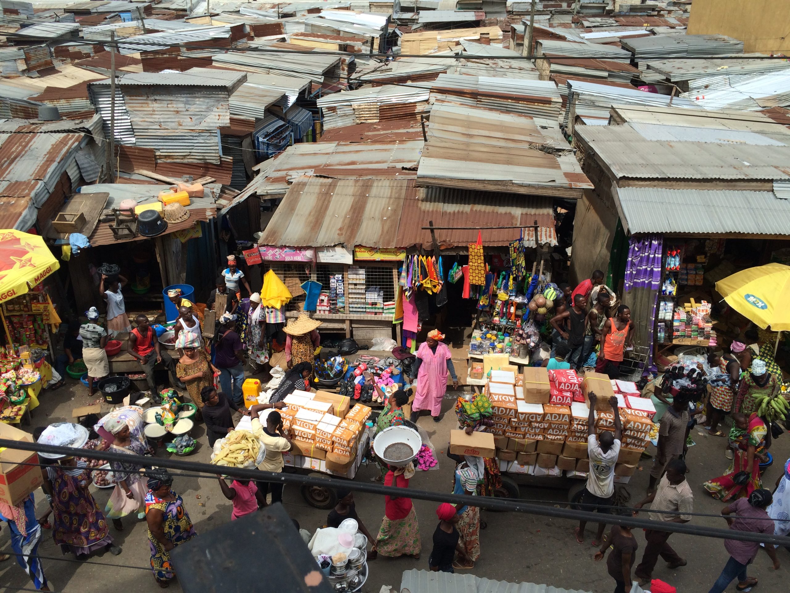 Goods, market traders, and corrugated iron stalls at Kumasi Central Market.