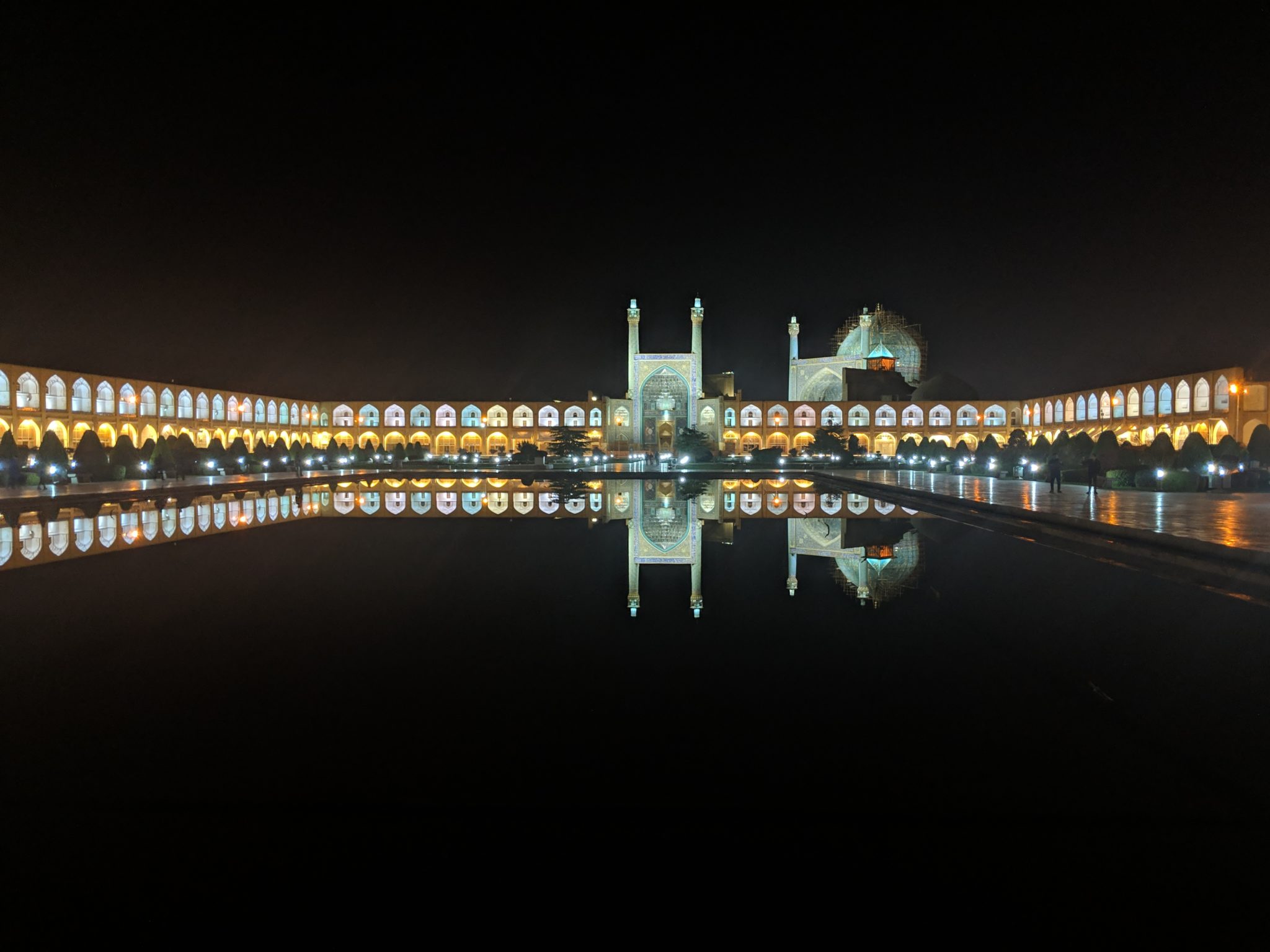 A large public square and mosque lit at night with pink, golden, and turquoise lights.