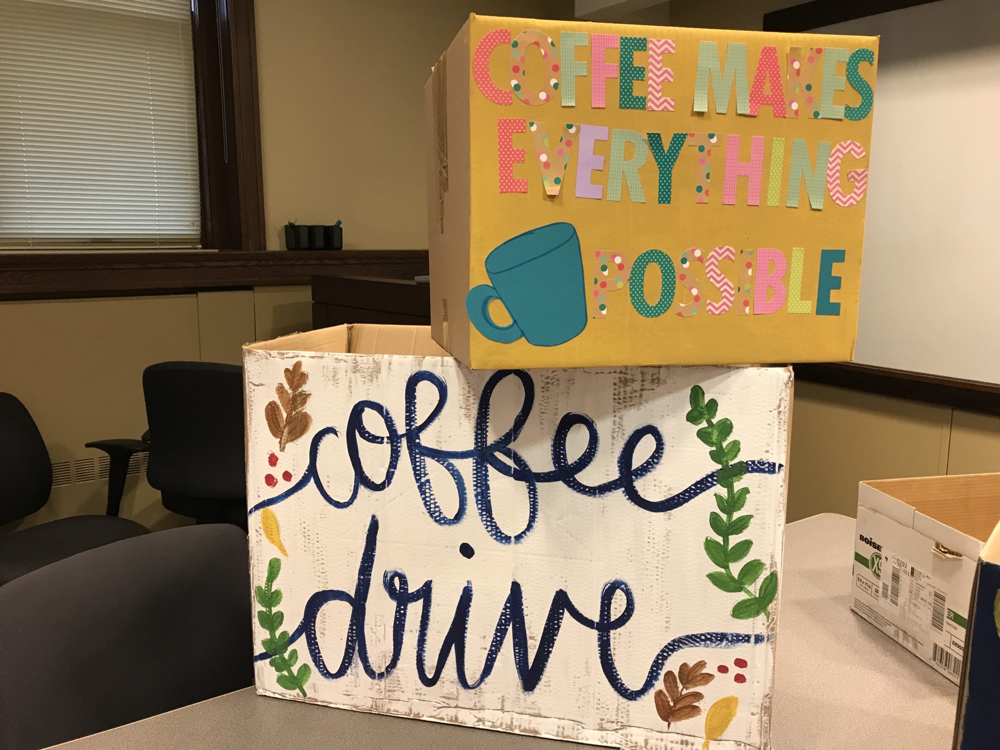 Two decorated cardboard boxes for the collection of donated coffee are stacked on a table