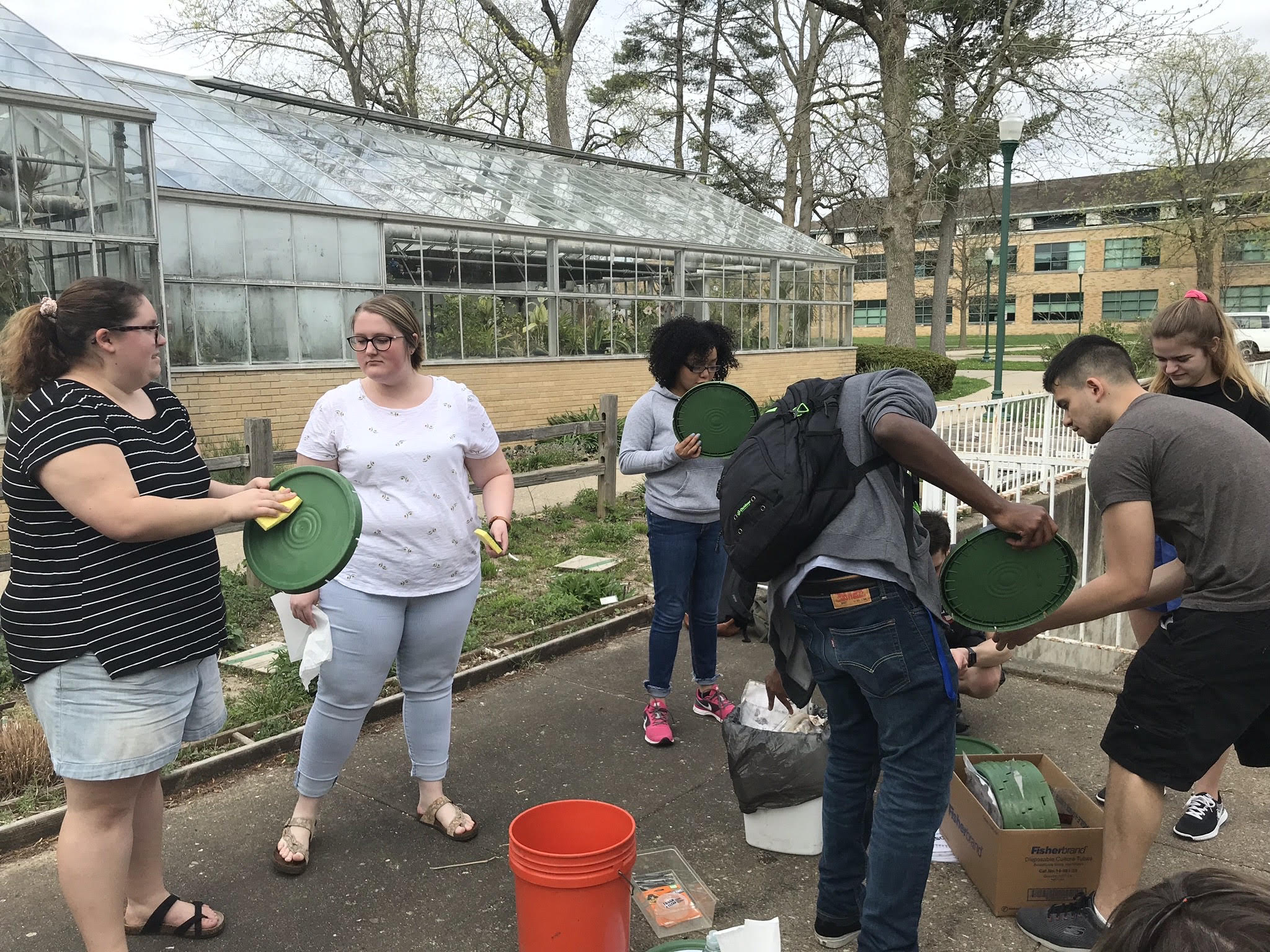 Six students stand outside and clean compost bucket lids