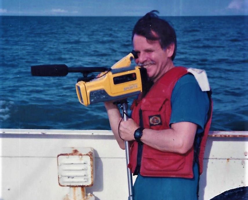 Photograph of a person on a boat holding a video camera.