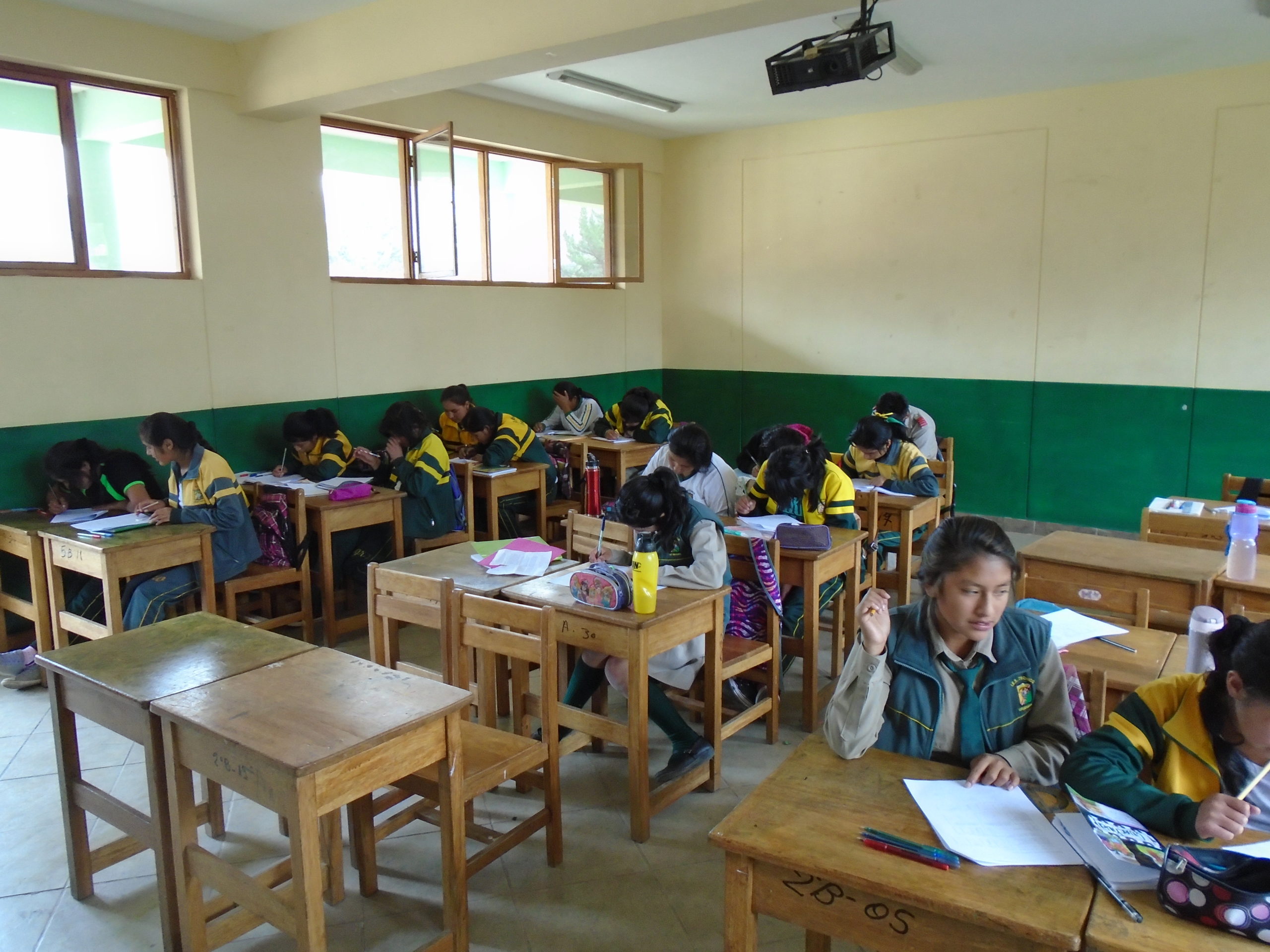 Picture of Peruvian students in a classroom with bare walls and wood desks.