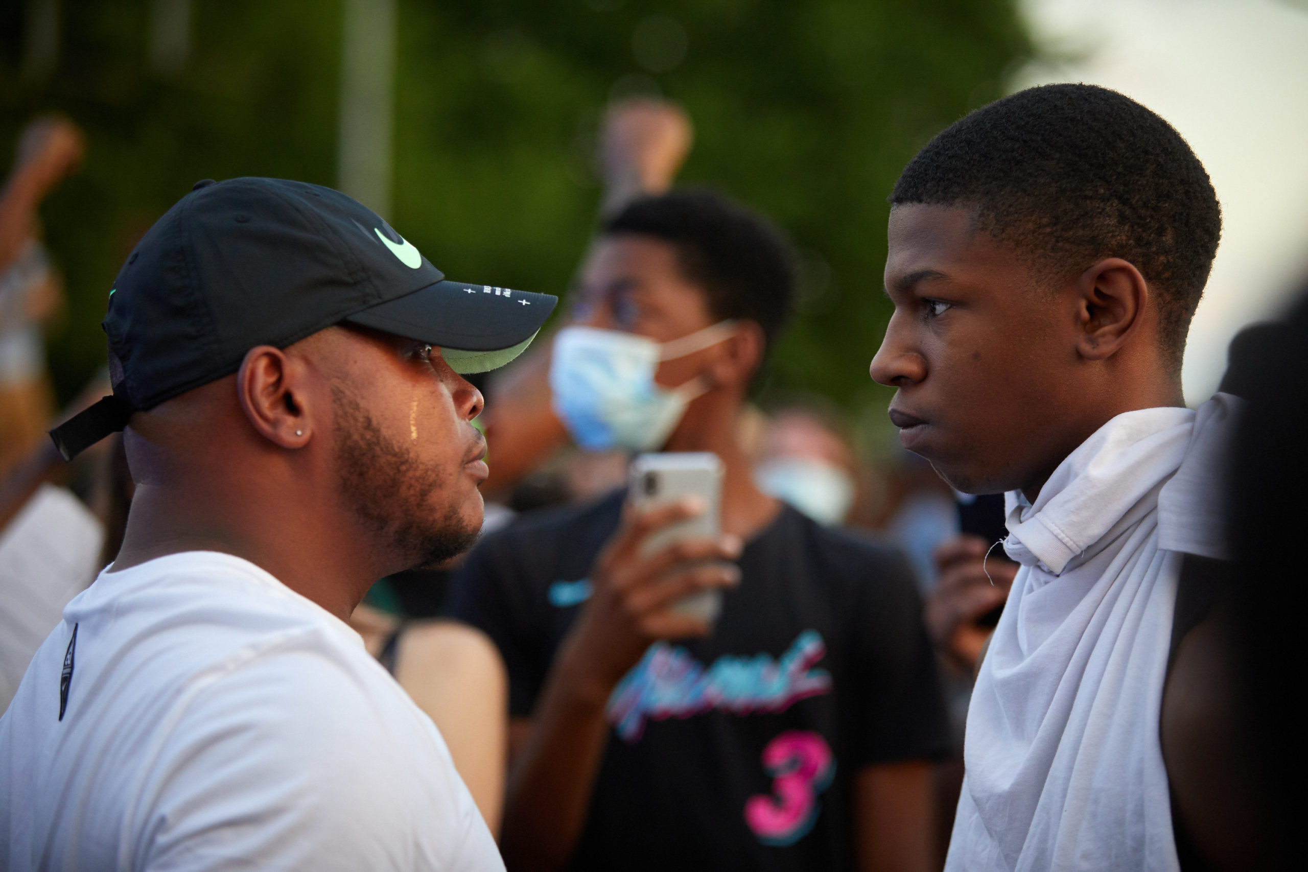 Photograph of two Black men in profile facing and talking to one another.