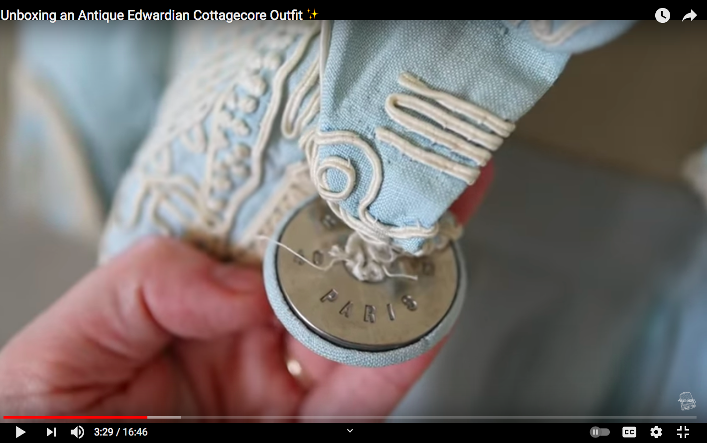 YouTube still of a metal button inscribed with the term 'Paris' on an Edwardian outfit